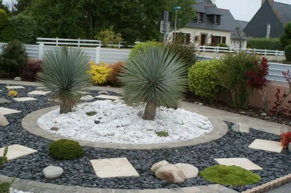Jardin Rocheux Moderne : Yuccas, Gravier Blanc et Ardoise Aménagement paysager moderne avec deux Yuccas bleus au centre, entourés de gravier blanc, délimité par des ardoises noires et des pas japonais.